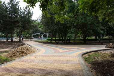 Parkta renkli beton döşeme döşemeleri. Profesyonel işçiler yeni kiremitler dikiyor ve seviyelendirilmiş kum temeline kaldırım döşemesi döşüyor..