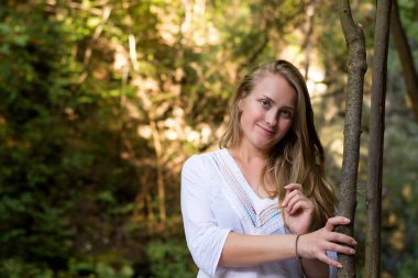 ormandaki doğada uzun sarışın ve dalgalı saçlı beyaz elbiseli güzel kız