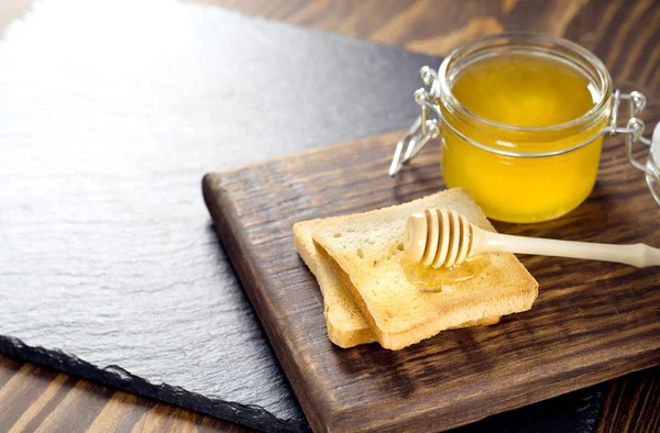 Sendok kayu dengan madu berbaring di atas sepotong roti di dekat botol madu — Stok Foto