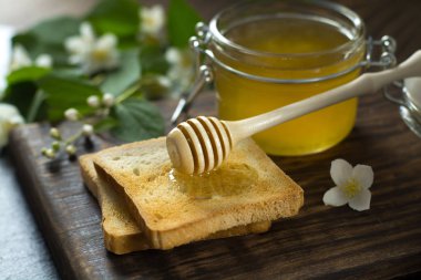 bal ile ahşap kaşık bal bir cam kavanoz yakın bir parça ekmek üzerinde yatıyor