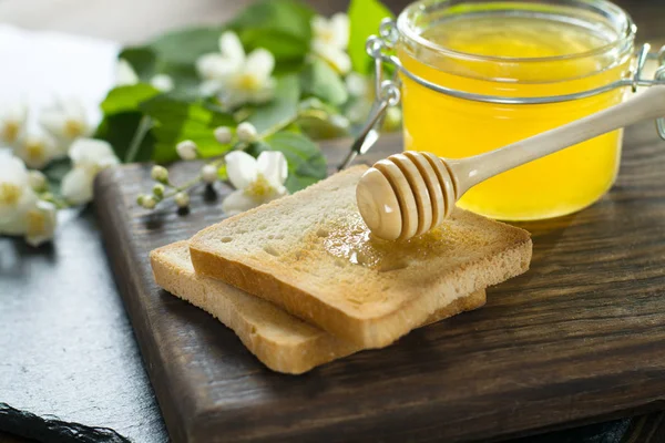 Cuchara de madera con miel está acostado en un pedazo de pan cerca de un frasco de vidrio de miel Imagen de archivo