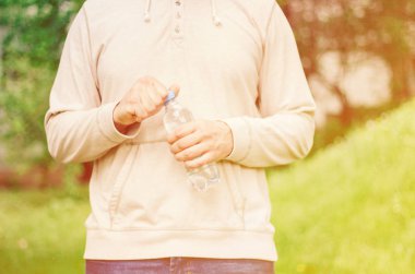 adam hipster doğada su ile plastik bir şişe tutan. sağlıklı yaşam tarzı, yaz, ısı. Parkta yürüyün.