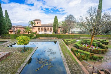 Tarihi Alhambra kompleksi içindeki Partal Gardens 'ın çarpıcı manzarası. Sakin gölet, yemyeşil çitler ve güzel Nasrid mimarisi mükemmel bir görüntü oluşturur..