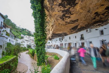 Setenil de las Bodegas, İspanya - 11 Mart 2025: Turistler Trejo Nehri 'nin yanındaki ünlü mağara kasabasının sokaklarında yürüyorlar. Köy, kayaların içine inşa edilmiş evleriyle tanınır..