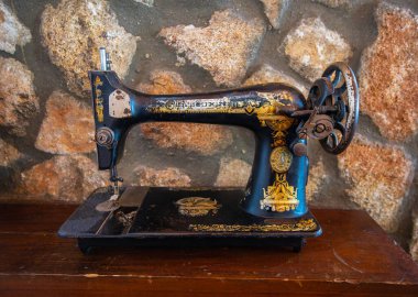 Setenil de las Bodegas, İspanya - 11 Mart 2025: Ahşap yüzeyine altın içeren antika siyah dikiş makinesi. Taştan arka planı olan yerel bir restoranda kırsal dekor..