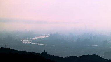 Tayvan 'daki Dadao Dağı' ndan Taipei şehrinin üzerinde rüya gibi bir şafak. Turuncu, pembe ve beyaz bulutlar şehir manzarası üzerinde mistik bir sis oluşturur..