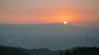 Tayvan 'daki Dadao Dağı' ndan gelen sisli bir şehrin üzerinde gün doğumu. Güneş bulutların arkasından doğar, dağların katmanları ve canlı turuncu gökyüzü ile rüya gibi bir sahne yaratır..