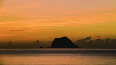 Sakin deniz ve kayalık kıyı üzerinde rüya gibi turuncu, pembe ve beyaz bulutlarla sonbahar şafağı erken saatlerde, Wanli, New Taipei City, Tayvan 'dan çekilen Keelung Adası..