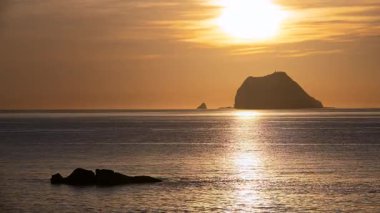 Güneş Keelung Adası 'nın arkasında yükselirken, sakin deniz ve kayalık kıyılar üzerinde turuncu, pembe ve beyaz bulutların yer aldığı sonbahar şafağı, Wanli, New Taipei City, Tayvan' dan çekildi..