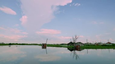 Reflections of sky and buildings shimmer on calm water near Sanjianwu. A leafless tree adds quiet contrast. Dongshi Township, Taiwan.