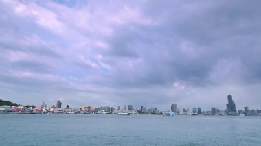 A busy scene of Kaohsiung Harbor and Gushan Ferry Pier in Taiwan with passenger ferries crossing the water to Cijin under a partly cloudy sky