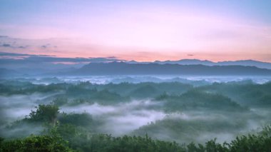 Aerial view of sunrise illuminating misty forests and rolling hills in Er Liao Zuozhen District Tainan Taiwan. Golden light pierces fog creating a serene sea of clouds atmosphere.