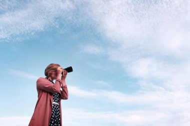 Bir kız bir kamera bir bulut arka planda tutuyor
