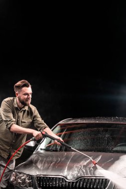 Bir adamla bir sakal veya araba yıkama oto yıkama gece yüksek basınç aparatı ile gri araba yıkar
