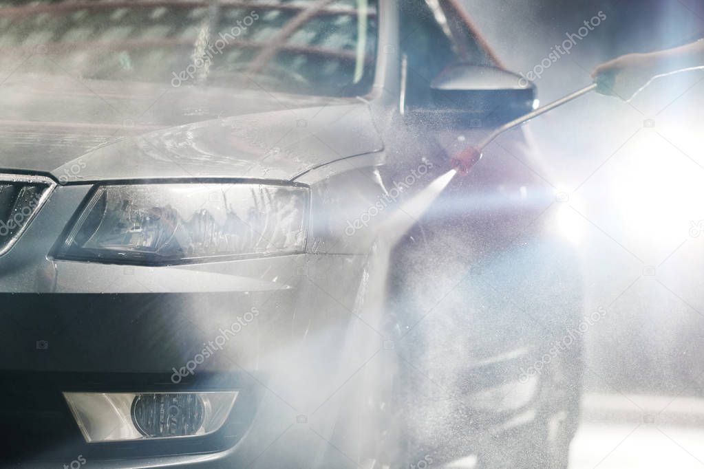 The car washer washes the grey automobile with a high-pressure device with studio light close up