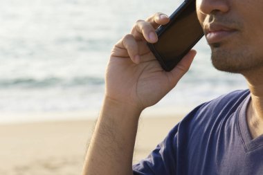 Tatil ve teknoloji. Deniz kıyısında smartphone kullanarak gündelik elbise genç Asyalı yakışıklı adam.