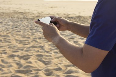 Tatil ve teknoloji. Deniz kıyısında smartphone kullanarak gündelik elbise genç Asyalı yakışıklı adam.