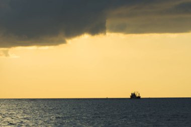 Alacakaranlık zamanında dramatik gökyüzü ile denizde gemi silueti.