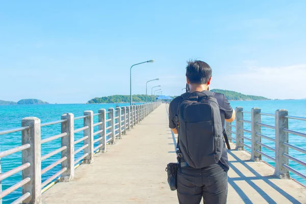 Fotografie und Reisen. junger Mann mit Rucksack steht auf Fischersteg und fotografiert wunderschönen tropischen Meerblick. — Stockfoto