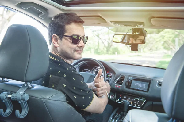 Guapo conductor asiático hombre sentarse en coche vuelta cuerpo atrás con sonrisa y pulgar hacia arriba . — Foto de Stock