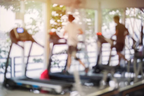 Centro de fitness borroso con máquinas cardiovasculares y peso, equipo de entrenamiento de fuerza. Figuras de humanos corriendo en cintas de correr en el gimnasio . —  Fotos de Stock