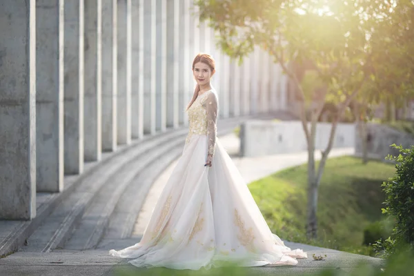 Beaux portraits avec lumière naturelle femme asiatique mariée en robe de mariée dans la nature prairie fleur, debout dans le champ vert herbeux en arrière-plan . — Photo