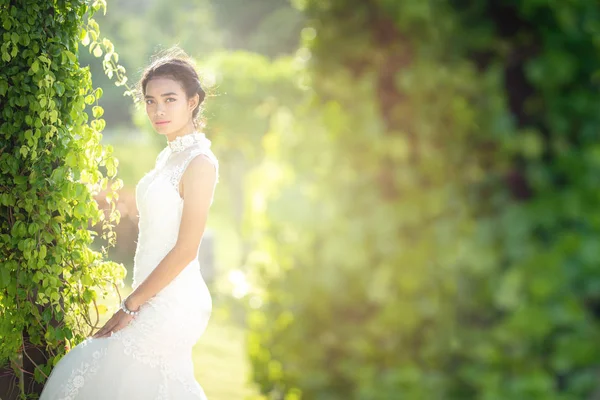 Beaux portraits avec lumière naturelle femme asiatique mariée en robe de mariée dans la nature prairie fleur, debout dans le champ vert herbeux en arrière-plan . — Photo