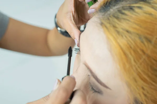 Makyaj sanatçısı asyalı kadın kıvırma fırçası kullanarak kirpikler üzerinde kozmetik maskara uygulayarak. — Stok fotoğraf
