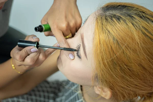 Makeup artist asian woman applying cosmetic mascara on eyelashes using curling brush. — Stock Photo, Image