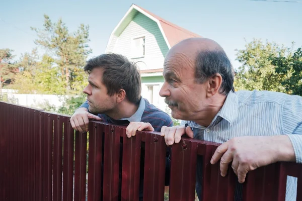 two caucasian men carefully watching over the fence.