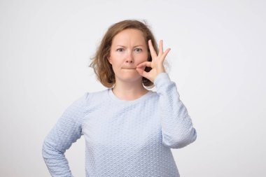 Genç Avrupalı Bayan closinge ağzını tarihlerde fermuar üstünde gri arka plan üzerinde. O gizli tutabilir gösteriyor.