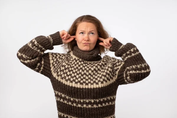 Kulakları tıkalı ve gürültüden rahatsız yüzü çatık sıcak kahverengi kazaklı genç erkek. Yüksek bir ses ve gürültü yorgun sakin rahat yerde kalmak istiyor