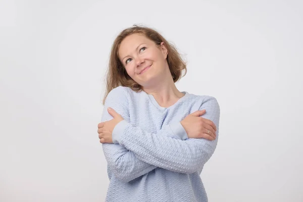 Portrait of middle aged pretty woman in blue sweater pretending like she is hugging herself. — Stock Photo, Image