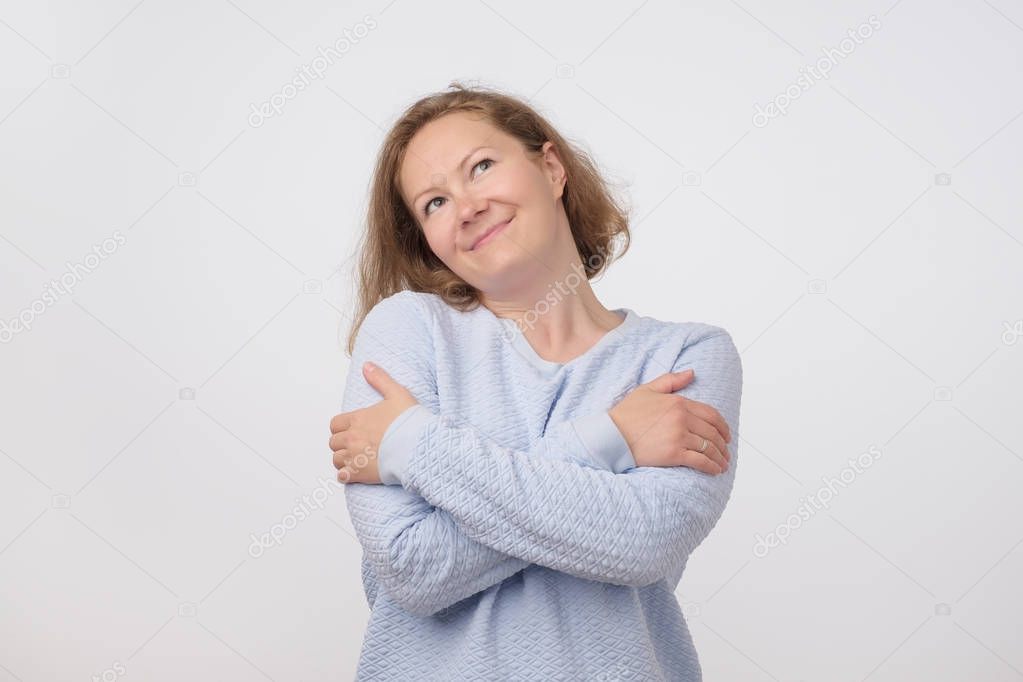 Portrait of middle aged pretty woman in blue sweater pretending like she is hugging herself.