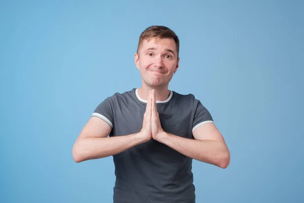 Knappe jongeman in blauw t-shirt pressings palmen samen en kijken naar camera, bedelen om vergeving — Stockfoto