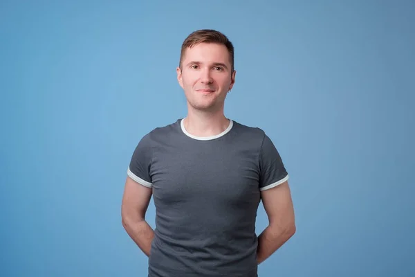 Zelfverzekerde jonge knappe man houden van armen gekruist en glimlachen terwijl je tegen blauw witte achtergrond — Stockfoto