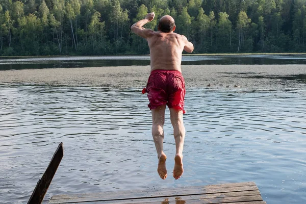 Mature man in red swimming clothes jumping into lake. having a good rest outdoor in vullage
