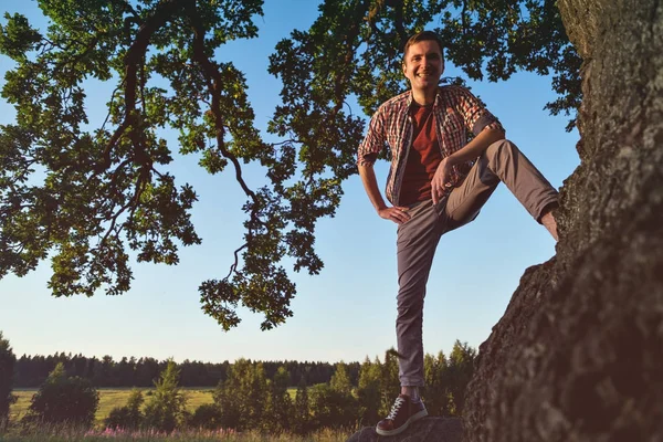 Мужчина в клетчатой рубашке стоит рядом с деревом и смотрит в сторону долины . — стоковое фото