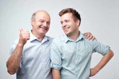 Senior father is proud of his mature son. He is pointing on him saying it is my boy. clipart