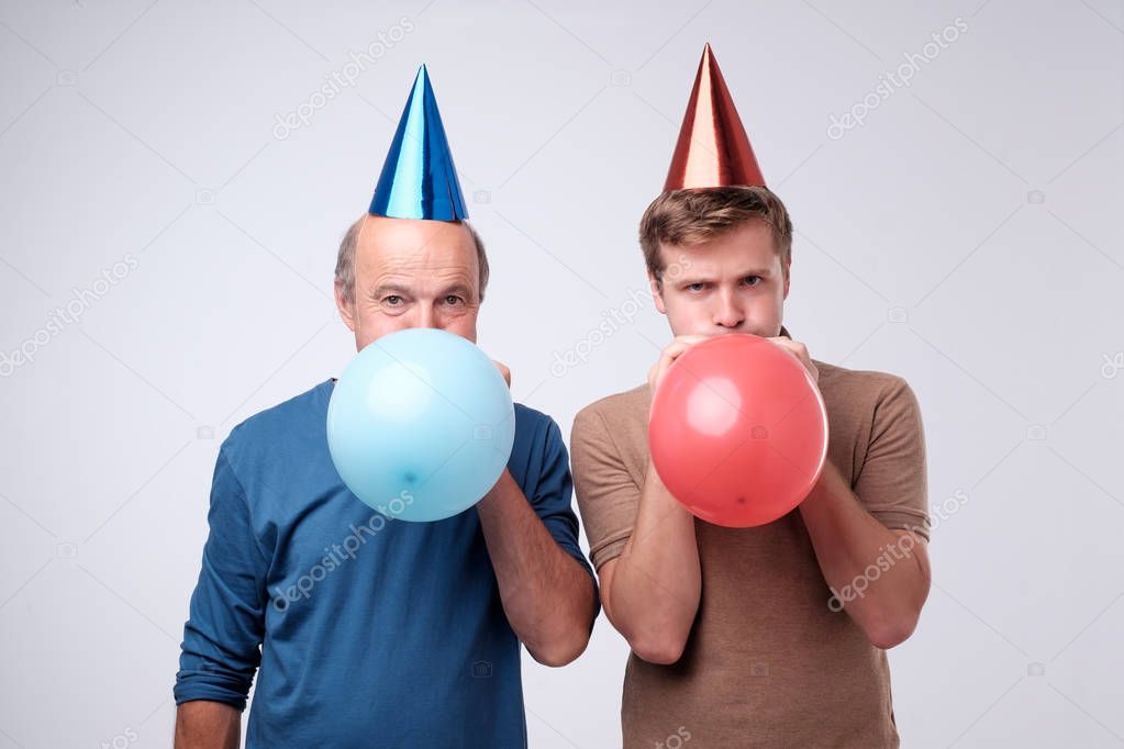 Mature and young men blowing up a balloon for birthday party isolated on white background