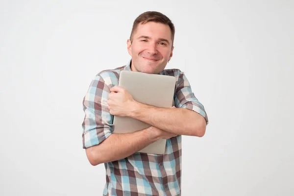 Портрет впевненого молодого чоловіка, що тримає ноутбук, що стоїть на білій стіні . — стокове фото