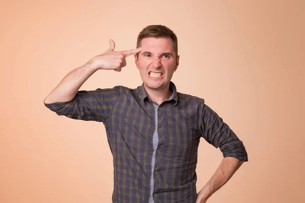 Tired or bored european guy holding gun gesture near temples and making faces while standing over orange background. — Stock Photo, Image