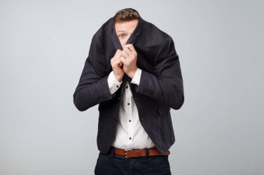 Riskli bir iş takım elbise, gri arka plan üzerinde onun yüzünden korkuyor genç iş adamı gizler.