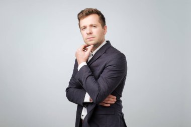 Yakışıklı genç işadamı abour gri arka plan karşı onun iş ayakta düşünme
