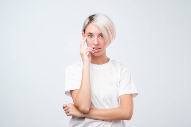 Beyaz tişört kısa renkli saçlı güzel genç kadın kameraya bakarak ve planlama yakınındaki ağız, elini tutuyor.