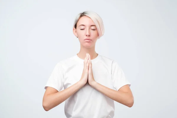 Молодая улыбающаяся женщина с короткой цветной прической медитирует, держа руки в жесте йоги, чувствуя себя спокойно — стоковое фото