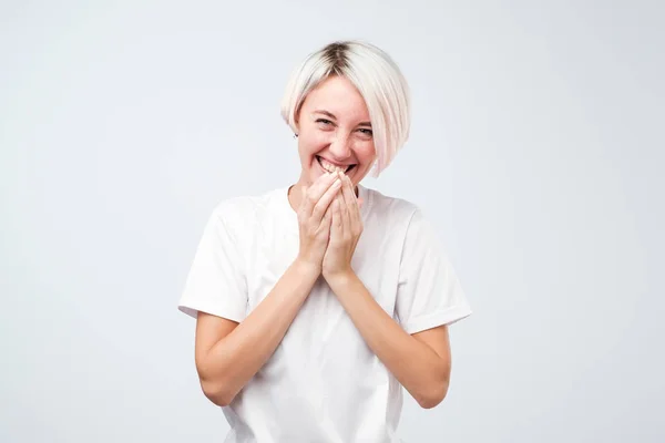 Belle jeune femme aux cheveux teints portant un t-shirt blanc rit joyeusement, couvre la bouche alors que les essais cessent de rire — Photo