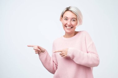 Gülümseyen genç kadın uzak gri bir arka plan üzerinde izole parmak işaret. Bak burada, sen bu satış kaçırılmaz