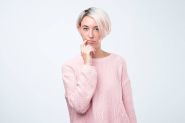 Pembe kazaklı güzel genç kadın elini ağzına yakın tutarak, kameraya bakıyor ve planlama.