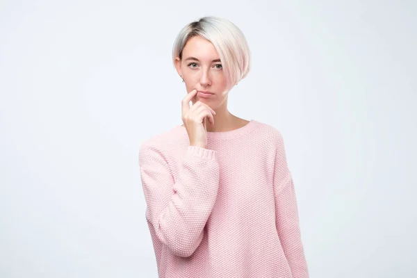 Красивая молодая женщина в розовом свитере держит руку у рта, смотрит в камеру и планирует . — стоковое фото